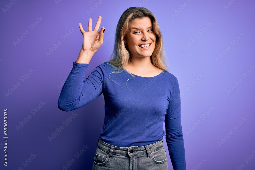 Fototapeta premium Young beautiful blonde woman wearing casual t-shirt over isolated purple background smiling positive doing ok sign with hand and fingers. Successful expression.