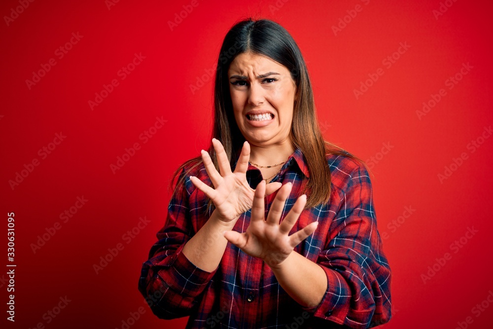 Young beautiful woman wearing casual shirt over red background disgusted expression, displeased and fearful doing disgust face because aversion reaction. With hands raised Young beautiful woman wearing casual shirt over red background disgusted expression, displeased and fearful doing disgust face because aversion reaction. With hands raised