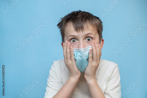 terrified boy in medical protective mask grabbed face with hands. hild with flu, influenza or cold protected from viruses, in bad epidemic situation, among patients with coronavirus