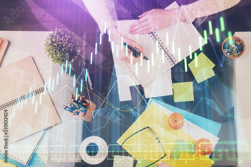 Hand taking notes in notepad. Forex chart holograms in front. Concept of research. Double exposure