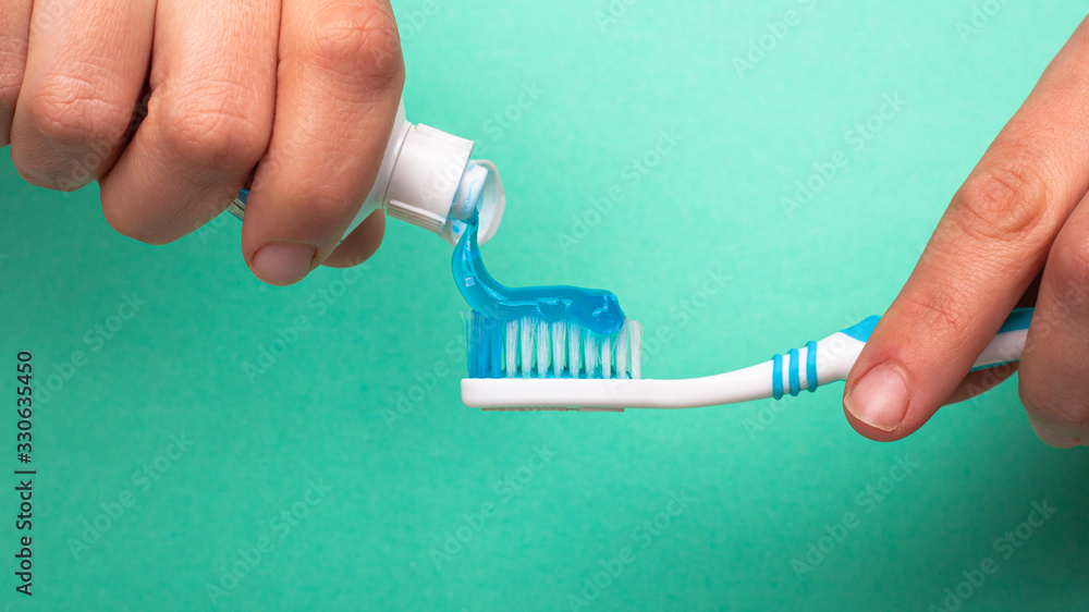 hand squeezes toothpaste onto a toothbrush on a turquoise background close-up. caries prevention and oral care hand squeezes toothpaste onto a toothbrush on a turquoise background close-up. caries prevention and oral care