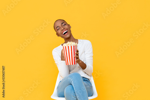 Happy young African American woman laughing while watching movie with popcorn...