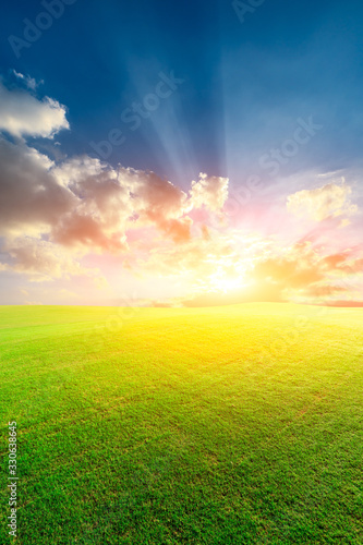 Green grass field and colorful sky clouds at sunset.