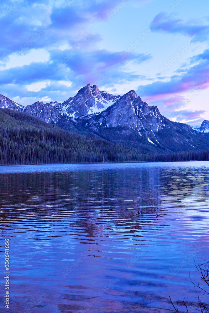 Purple mountain majesty jutting out of blue glacial lake with blue and purple sky