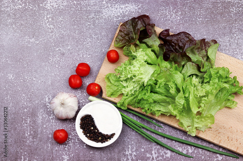 Leaf lettuce with cherry tomatoes, green onions and garlic on a wooden board on a dark wooden background. Top view, flat lay