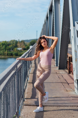 Pretty young woman posing on the old rusty transport bridge over the river during sunset.