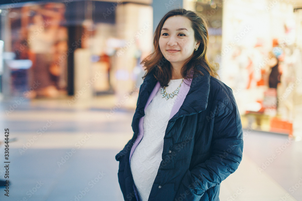 a pregnant woman is stroking her stomach. a girl waiting for a child walks in a shopping center. The concept of a healthy lifestyle , IVF, fashion for pregnant women, children a pregnant woman is stroking her stomach. a girl waiting for a child walks in a shopping center. The concept of a healthy lifestyle , IVF, fashion for pregnant women, children