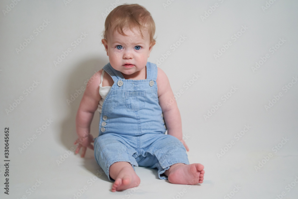 emotional portrait of a one-year-old baby in denim overalls on a uniform light background emotional portrait of a one-year-old baby in denim overalls on a uniform light background