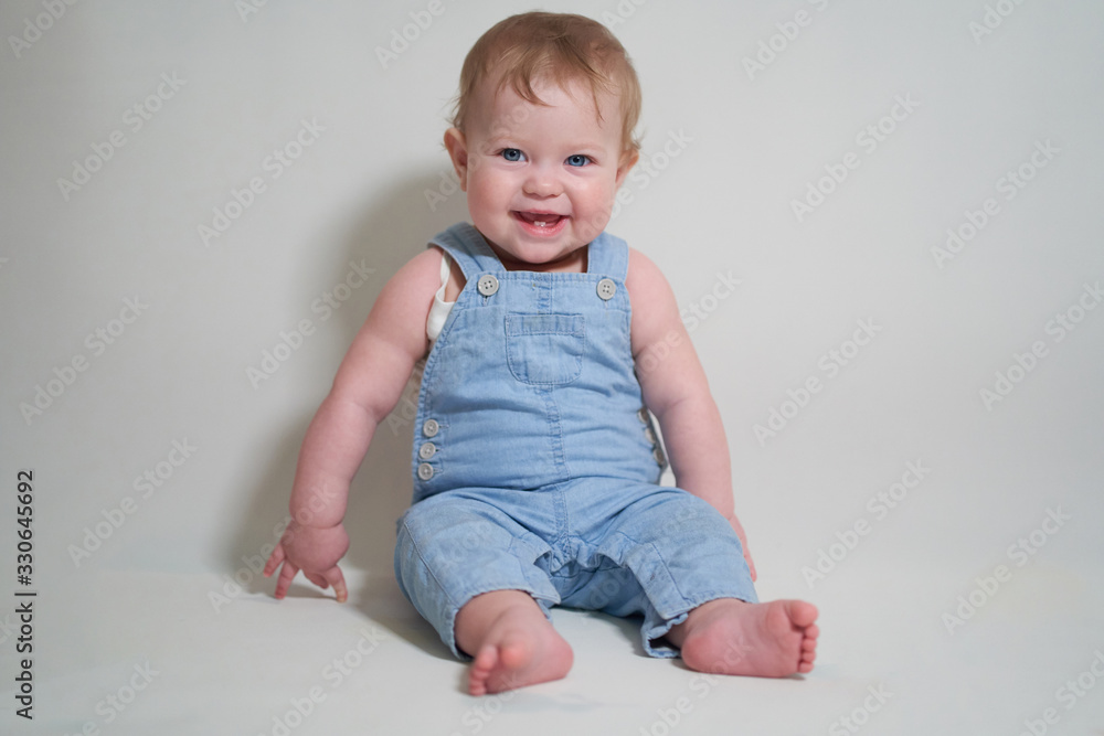 emotional portrait of a one-year-old baby in denim overalls on a uniform light background emotional portrait of a one-year-old baby in denim overalls on a uniform light background