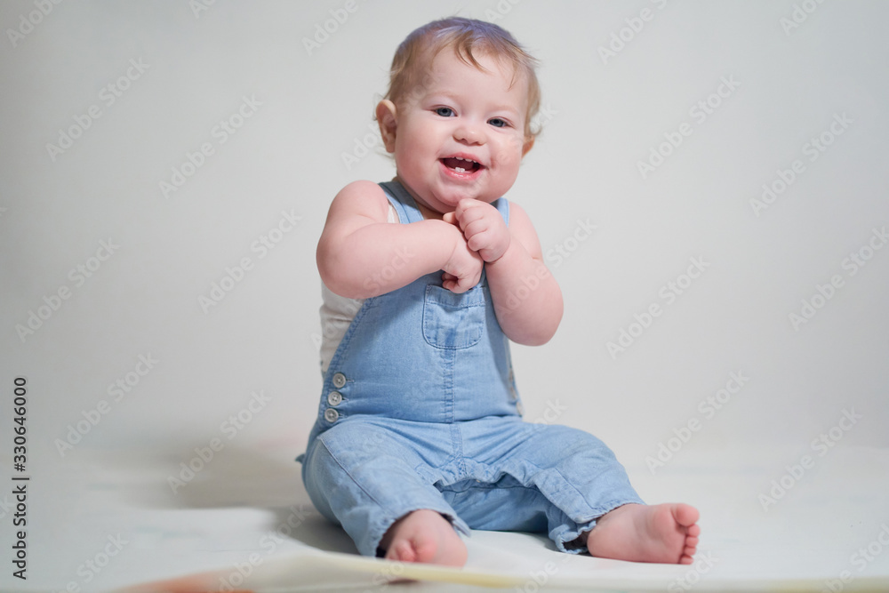 emotional portrait of a one-year-old baby in denim overalls on a uniform light background emotional portrait of a one-year-old baby in denim overalls on a uniform light background