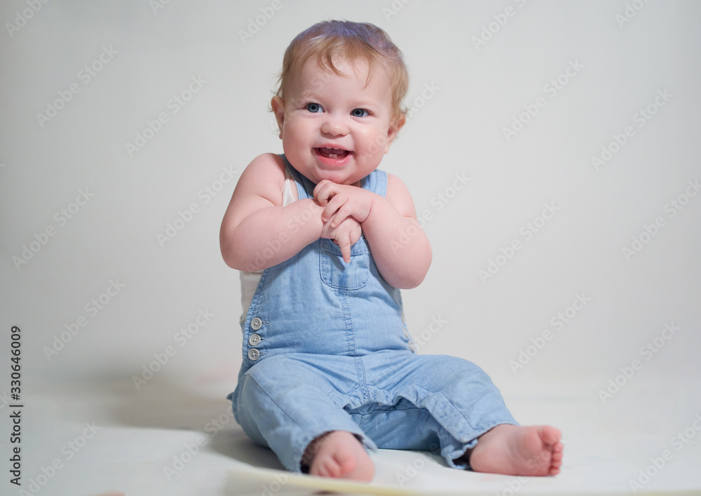 emotional portrait of a one-year-old baby in denim overalls on a uniform light background emotional portrait of a one-year-old baby in denim overalls on a uniform light background
