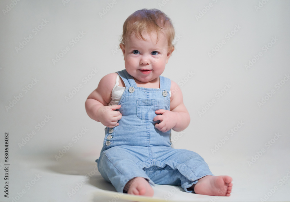 emotional portrait of a one-year-old baby in denim overalls on a uniform light background emotional portrait of a one-year-old baby in denim overalls on a uniform light background