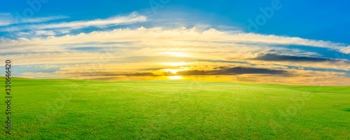 Green grass field and colorful sky clouds at sunset panoramic view.