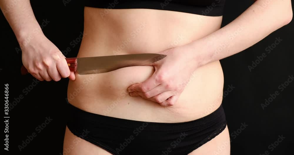 The concept of getting rid of excess weight. Girl cuts off fat deposits with belly knife/ The concept of getting rid of excess weight. Girl cuts off fat deposits with belly knife/