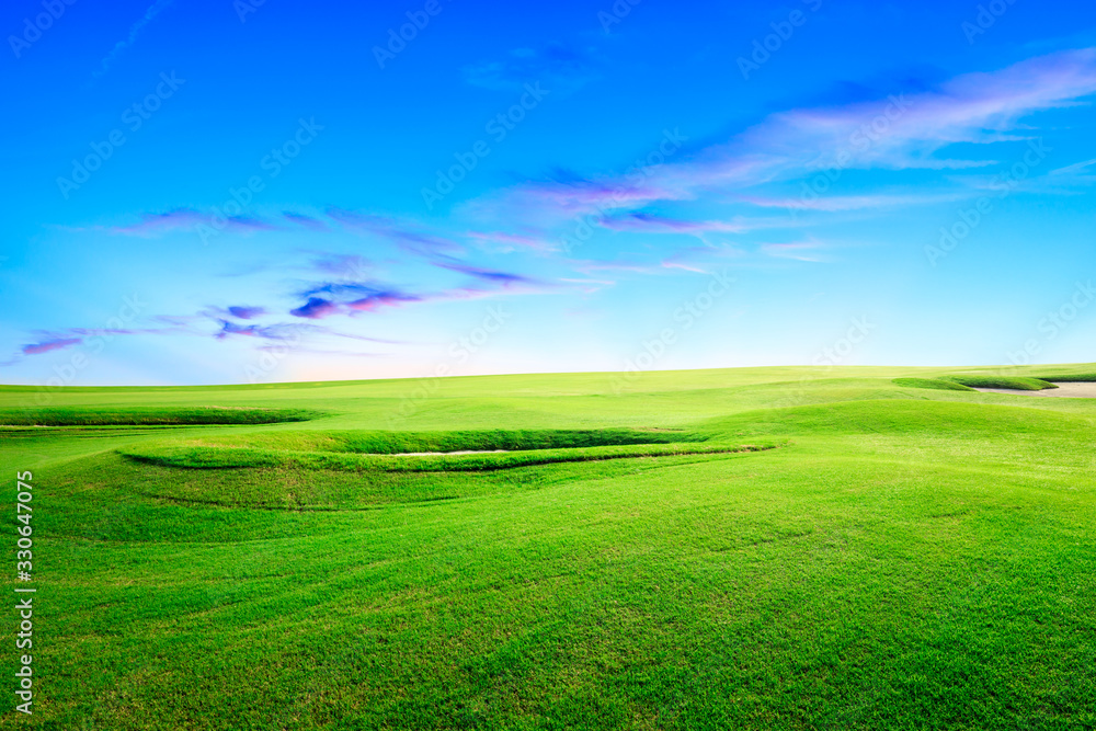Fototapeta premium Green grass field and colorful sky clouds at sunset.
