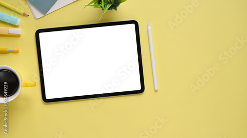 Top view image of colorful working table with accessories putting on it. Flat lay Computer tablet with white blank screen, stylus pen, marker pen, notebook, diary, coffee cup and potted plant.