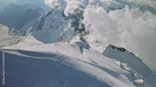 Fabulous light clouds float under snow summit, climbers conquer mountain top