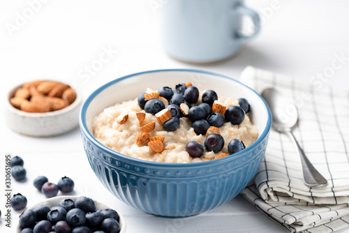 Bowl of oatmeal porridge with blueberries and almond nuts on white table. Healthy breakfast food, clean eating concept