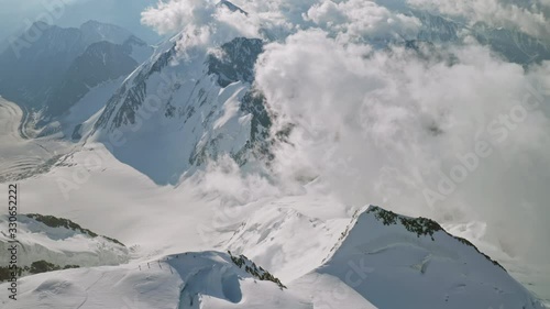 Magic alpine panorama, alpinists climbs on snow scarp, clouds float below summit photo