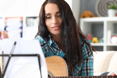 Musician looks at note for guitar on music stand. Training in reading from sheet notes for quick memorization composition. Music teacher reviews new material for playing instrument