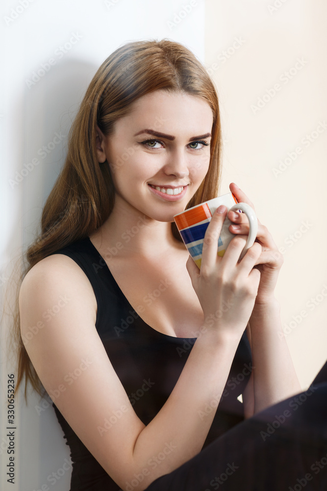Young woman with a cup sitting near window at home. Young woman with a cup sitting near window at home.