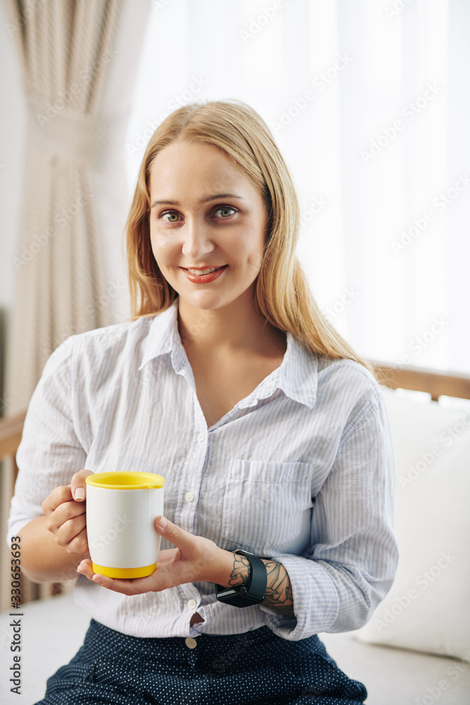 Portrait of pretty positive young woman holding cup of hot tea and looking at camera Portrait of pretty positive young woman holding cup of hot tea and looking at camera