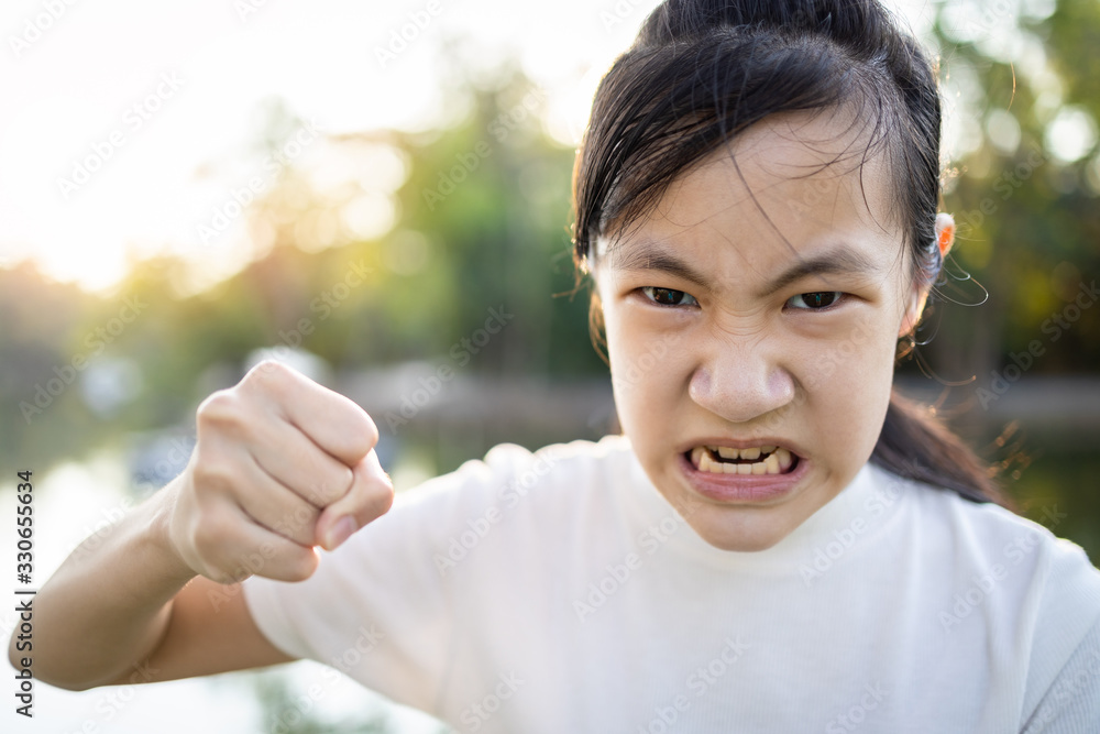 Serious asian child girl with her fist raised for threat warning or quarreling,angry female threatening with fist,about to punch,aggressive schoolgirl,facial expression,concept of aggression,bully Serious asian child girl with her fist raised for threat warning or quarreling,angry female threatening with fist,about to punch,aggressive schoolgirl,facial expression,concept of aggression,bully