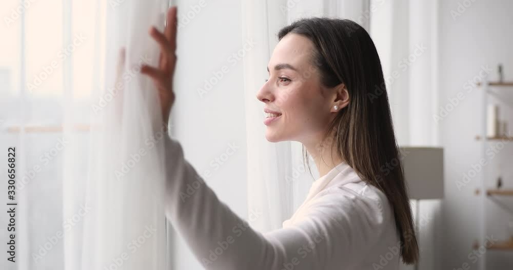 Happy young woman opens window lace looking outside apartment. Smiling mindful attractive lady watching beautiful cityscape view enjoying dreaming and contemplating feeling hope concept. Side view Happy young woman opens window lace looking outside apartment. Smiling mindful attractive lady watching beautiful cityscape view enjoying dreaming and contemplating feeling hope concept. Side view