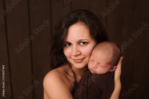 Young woman holding a newborn baby in her arms on the white background. Newborn photosession. Family portrait. Mother is kissing her baby. Baby goods packing template. Nursery. Medical and healthy.