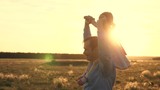 Dad with his beloved daughter on his shoulders dances in flight and laughs. Happy child plays with his father on sunset field. Silhouette of a man and a child. Family and Childhood Concept