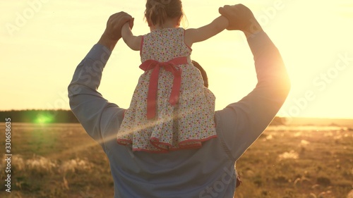 Dad with his beloved daughter on his shoulders dances in flight and laughs. Happy child plays with his father on sunset field. Silhouette of a man and a child. Family and Childhood Concept