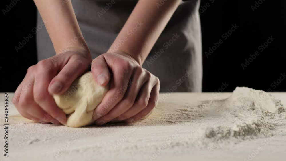 Professional baker kneads the dough on a wooden table near the heap of flour against black background. Concept of cooking delicious pizza. Middle shot. 4K Professional baker kneads the dough on a wooden table near the heap of flour against black background. Concept of cooking delicious pizza. Middle shot. 4K