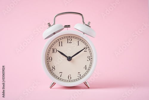 White retro alarm clock on the pink background with copy space. Time concept