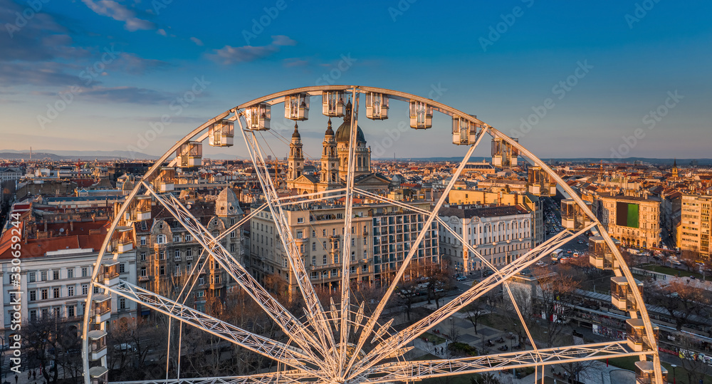Budapest, Hungary - Aerial panoramic view of the ferris wheel at Elisabeth Square (Erzsebet ter) at sunset with St. Stephen's Basilica and blue sky at background