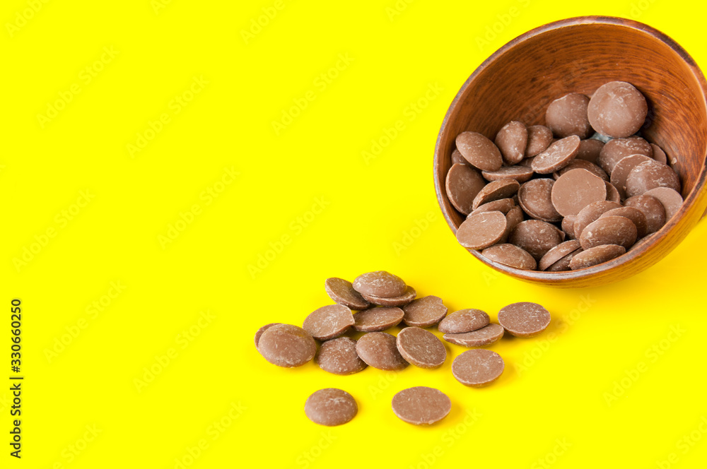 Drops of milk chocolate in a clay Cup on a yellow background Drops of milk chocolate in a clay Cup on a yellow background