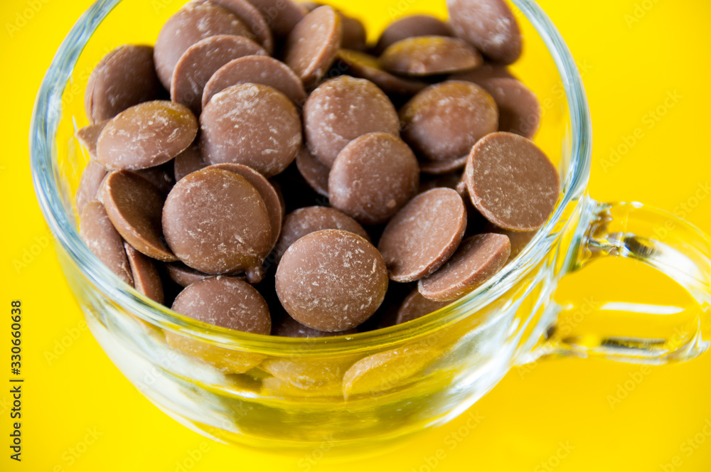 Fototapeta premium Drops of milk chocolate in a transparent Cup on a yellow background