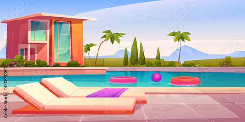 House and swimming pool with deck chairs on poolside and balls in water. Vector cartoon summer landscape with villa, basin on lawn, palms and mountains on background