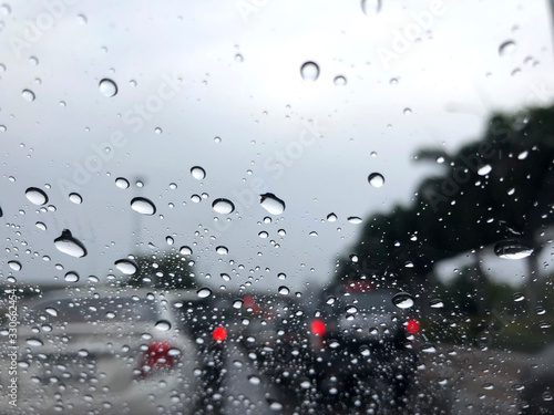 The raindrops that are stuck on the windshield have the backdrop of a road jammed with cars.
