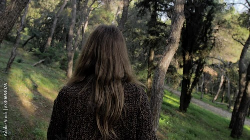 Young blonde woman walks on path among pine trees, turns to smile at the camera, gimbal following photo