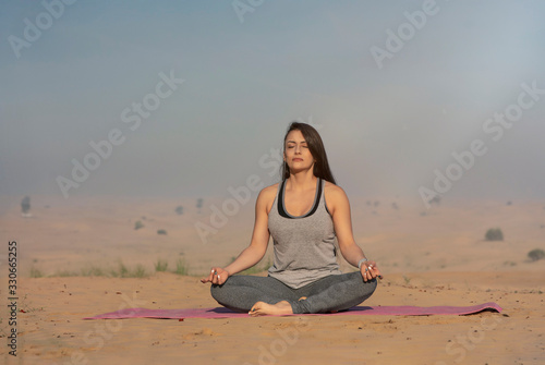 Beautiful Caucasian latin brunette woman performing yoga poses in the desert on a pink yoga mat in the Middle East 