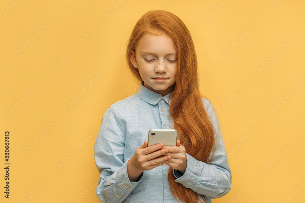 portrait of adorable caucasian red haired girl with mobile phone, pretty kid girl using smartphone, chatting with friend. isolated yellow background. modern technologies concept portrait of adorable caucasian red haired girl with mobile phone, pretty kid girl using smartphone, chatting with friend. isolated yellow background. modern technologies concept