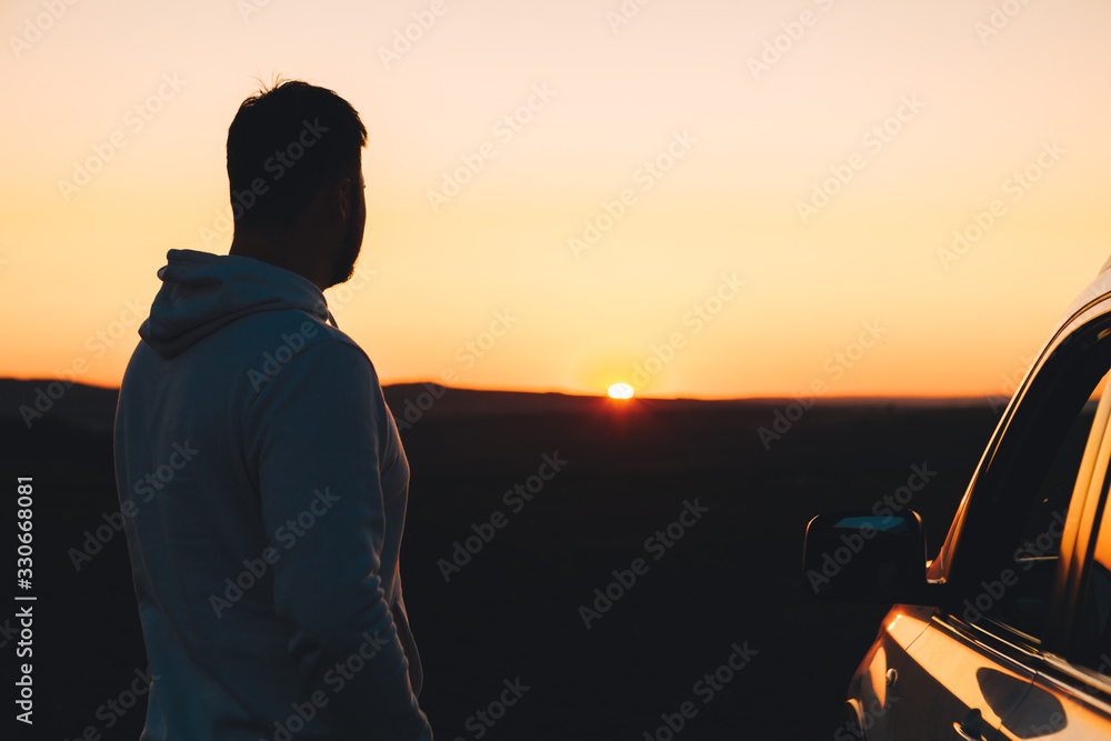 man standing near white suv car looking at sunset