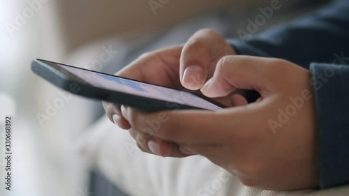 Side view. Hand of girl using smartphone in the living room at home,  typing message. Close-up of young women hand