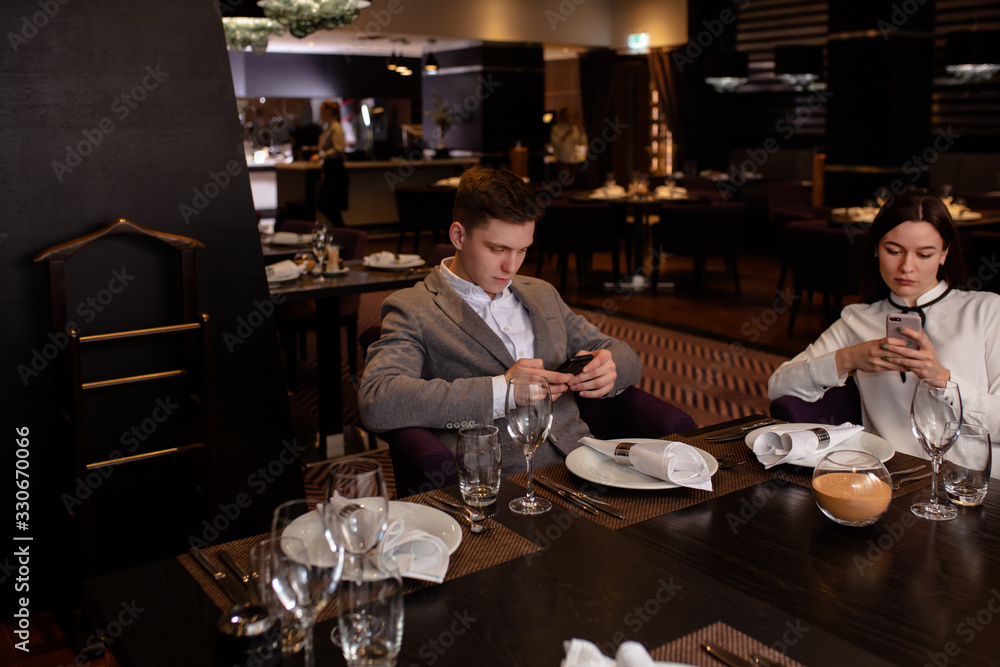 caucasian couple use mobile phone in restaurant. guy and lady came to have dinner together, but both of them busy with their work in mobile phones caucasian couple use mobile phone in restaurant. guy and lady came to have dinner together, but both of them busy with their work in mobile phones
