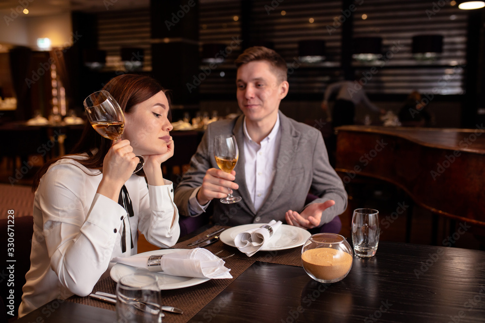 bored caucasian woman with champagne and handsome man entertaining her. male in love with her, while woman is not interested in rendezvous with him. in luxury restaurant