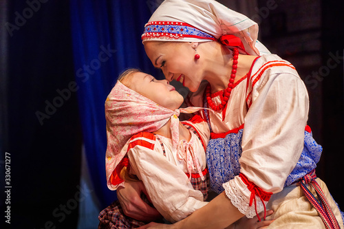 A little girl and an adult woman in Russian national dress posing during photoshoot on stage. Mother and daughter together
