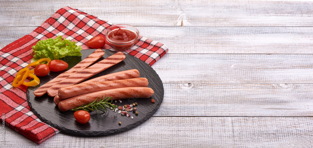 Grilled sausages with tomato sauce, spices and herbs on a stone plate, isolated on white background