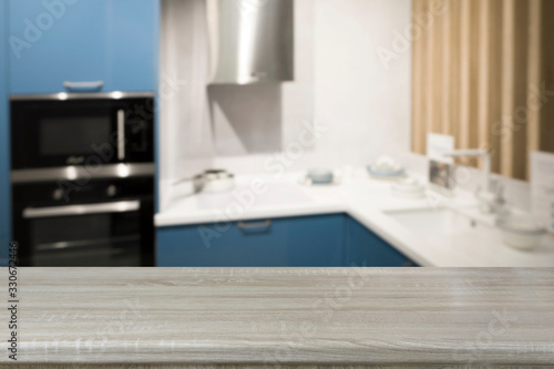 Empty wooden tabletop and defocused blue modern kitchen as background for design.