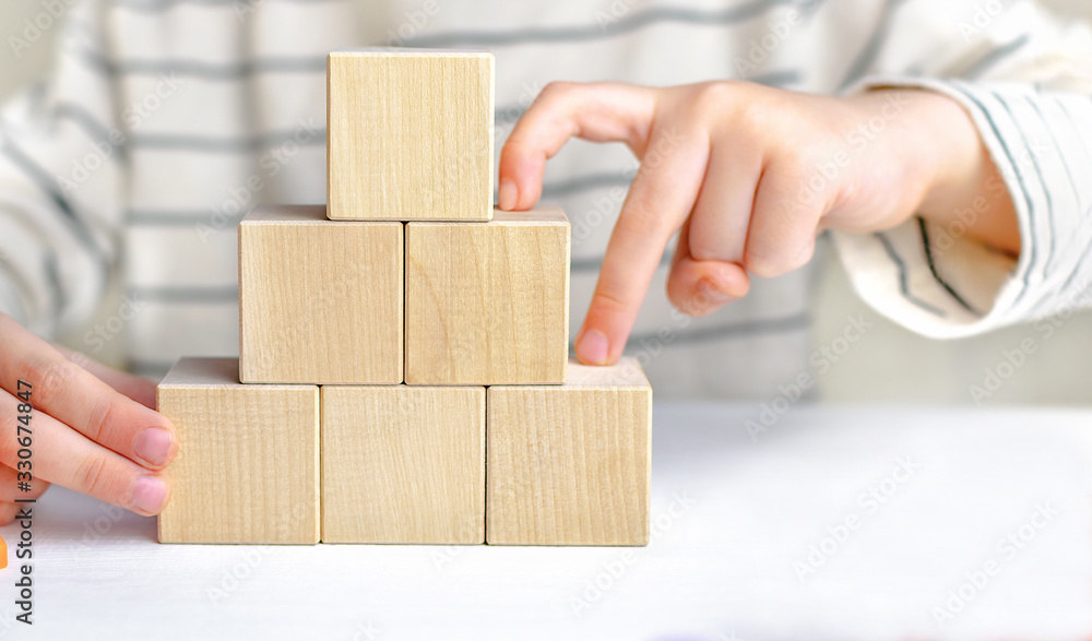 The childs hands build a staircase from cubes, fingers climbing the ladder up of wooden blocks. The concept of victory, the way to success, achieving goals, progress, motivation, ambition. The childs hands build a staircase from cubes, fingers climbing the ladder up of wooden blocks. The concept of victory, the way to success, achieving goals, progress, motivation, ambition.