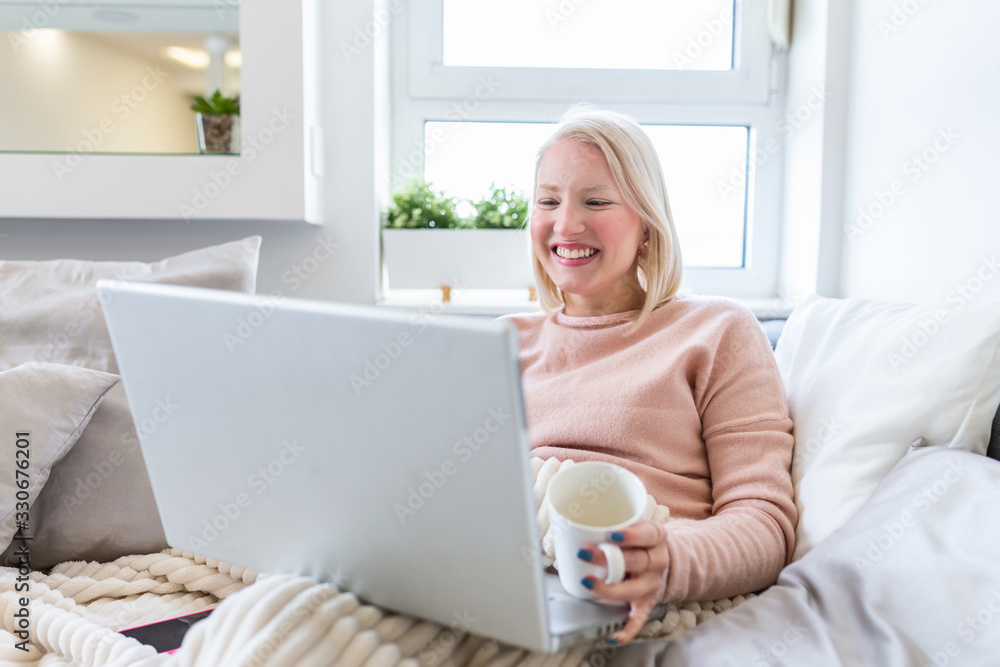 Young woman drinking coffee at home in her bed and checking her laptop. Beautiful young woman drinking coffee at home in her bed while working on her laptop. Checking email in the morning Young woman drinking coffee at home in her bed and checking her laptop. Beautiful young woman drinking coffee at home in her bed while working on her laptop. Checking email in the morning